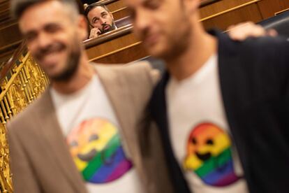 Dos diputados, con camisetas del fantasma con la bandera LGTBI que utilizó Vox durante la campaña de las elecciones generales, posan delante de Santiago Abascal.