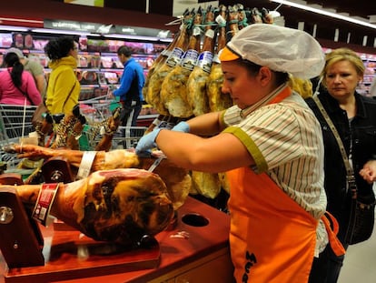 Una empleada cortando jamón en un supermercado.