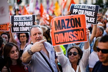 Un manifestante señala un cartel que pide la dimisión de Carlos Mazón sostenido por otra participante en la protesta de Valencia.
