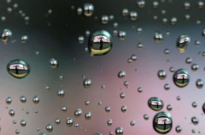 Gotas de lluvia en la ventanilla de un coche reflejan a un hombre que camina ante un panel con el índice de la bolsa de Tokio el 03 de abril 2014.