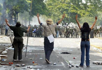 Tres manifestantes, frente a los efectivos policiales, durante los incidentes de ayer en Caracas.