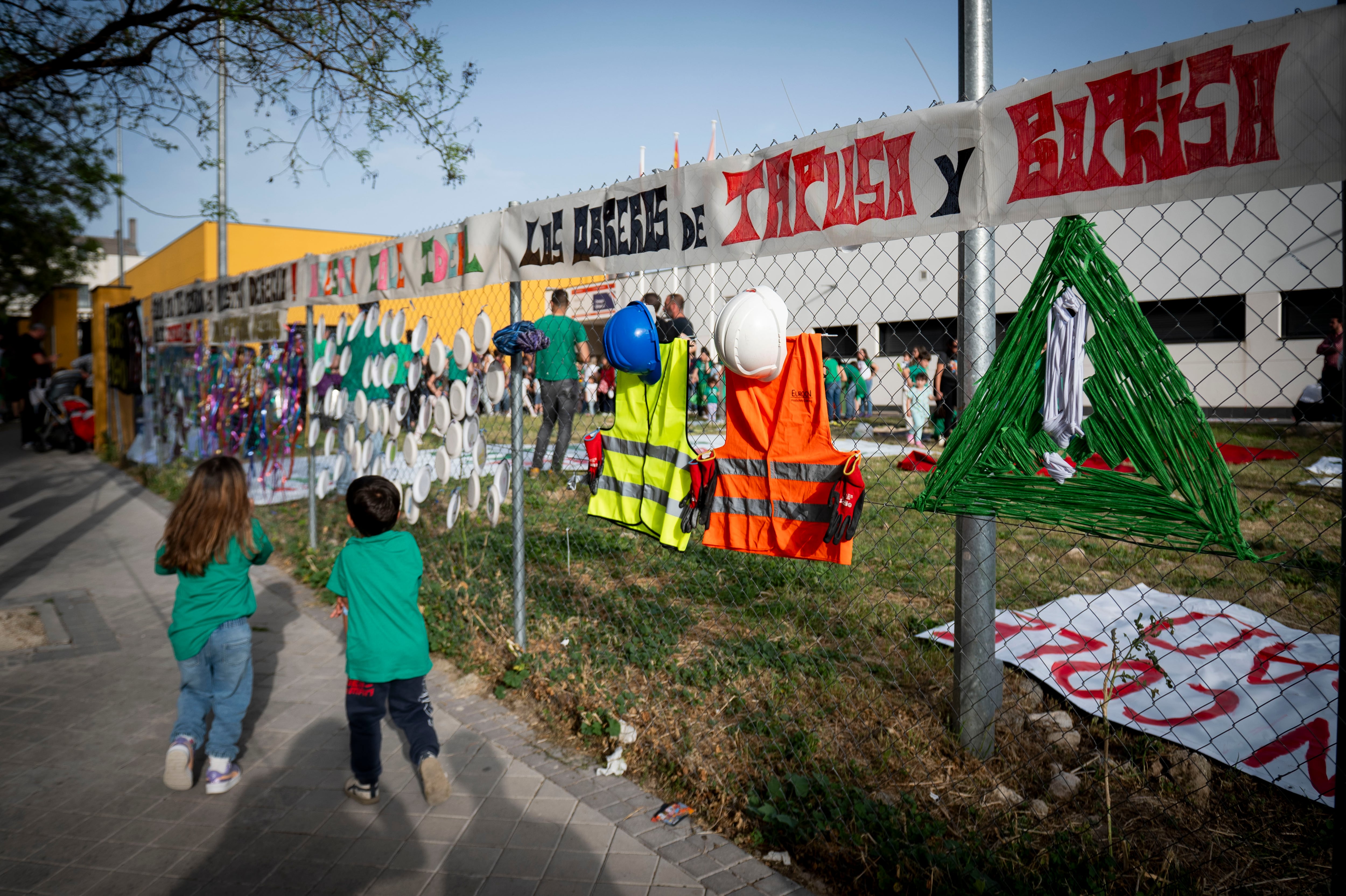 Dos niños corren alrededor del CEIP Hispanidad, lleno de carteles que piden que se terminen las obras.