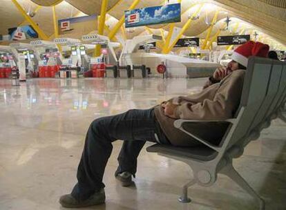 Sergio intenta dormir en un banco de la T4 donde se ha quedado colgado en Nochebuena por un vuelo cancelado de Ryan Air. 
/ ÁLVARO DE CÓZAR
Una pareja de Villagarcía y una familia argentina brindan en una improvisada cena  en el aeropuerto.