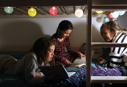 Dos niñas de nueve y 11 años leen un libro con su madre en su casa.