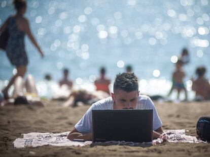 Una persona utiliza su ordenador en la playa de la Barceloneta.