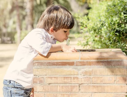 Un niño bebe agua de una fuente.