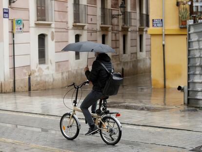 Un ciclista se protege de la lluvia con un paraguas, este jueves en Valencia.