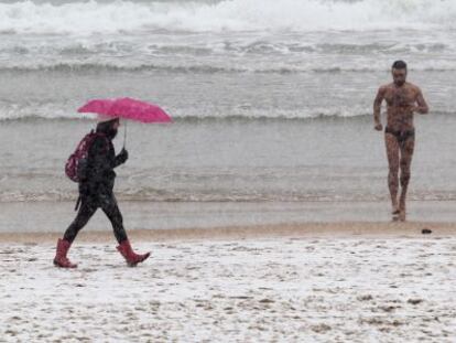 Un hombre en ba&ntilde;ador corre por una nevada playa de la Concha, en San Sebasti&aacute;n.