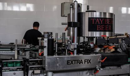 Un empleado revisa cajas tras la máquina encargada de poner las chapas a las botellas, en Taybeh, Ramala, Cisjordania, el pasado 17 de septiembre de 2019.