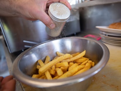 Un hombre echa sal en un recipiente con patatas fritas.