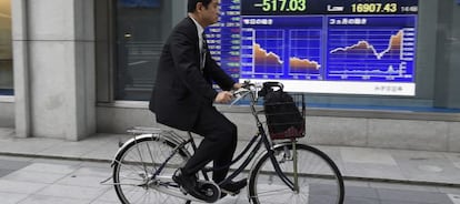 Un hombre pasa en bicicleta por delante de una pantalla con los datos de la bolsa de Tokio (Jap&oacute;n).