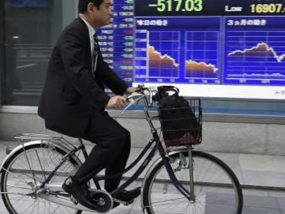 Un hombre pasa en bicicleta por delante de una pantalla con los datos de la bolsa de Tokio (Jap&oacute;n).