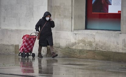 Una mujer con mascarilla camina bajo la lluvia con el carro de la compra durante el Martes Santo y la cuarta semana del estado de alarma decretado por el Gobierno por la crisis del coronavirus, en Pamplona.