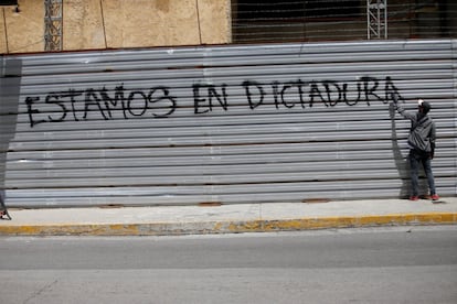 Un hombre pinta un grafiti sobre una pared donde se puede leer 'Estamos en dictadura'.