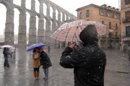 Varios turistas se fotografían en medio de una nevada junto al acueducto romano en la capital segoviana. EFE/Archivo