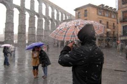 Varios turistas se fotografan en medio de una nevada junto al acueducto romano en la capital segoviana. EFE/Archivo