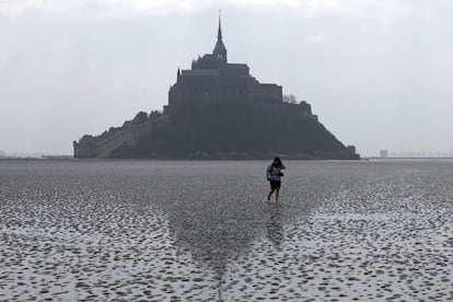 Una mujer camina por la arena frente al Monte Saint-Michel. La bajamar, que también es más fuerte de lo normal, deja expuestas áreas de playa y roca sólo visibles cada 18 años.