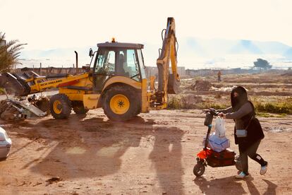 Una mujer transporta una maleta y una bolsa con sus pertenencias mientras una excavadora derriba las chabolas en el cortijo El Uno de San Isidro, en Njar (Almera).