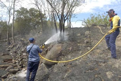 Dos miembros del Cuerpo de Bomberos de la Generalitat remojan la zona afectada por el incendio forestal declarado ayer en Sant Climent Sescebes.