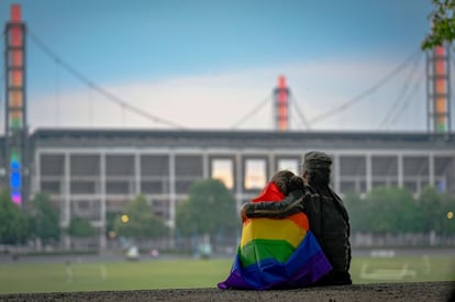 Dos personas envueltas en una bandera arcoíris se abrazan mientras observan el estadio Rheinenergie iluminado con los mismos colores, en Colonia, oeste de Alemania. Varios lugares del país se cubrieron con estos tonos como protesta contra las leyes anti-LGTBIQ+ de Hungría, en los días previos y posteriores al partido que la selección alemana jugaba contra la húngara.