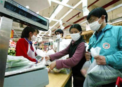Varias personas esperan con mascarillas su turno en un supermercado de Pekín.