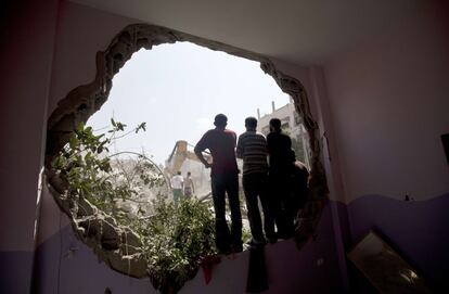 Palestinos miran al cielo desde el agujero en una pared de un edificio destruido en un ataque aéreo israelí en la ciudad de Gaza.