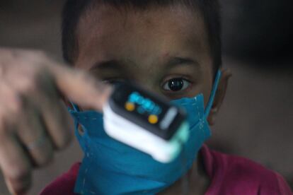 Un niño observa un oxímetro en la mano de un residente durante un chequeo médico en Dharavi (Mumbai, India).