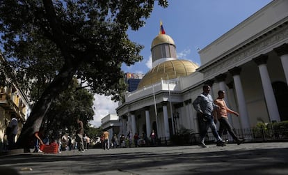 Dos personas caminan frente a la Asamblea Nacional de Venezuela.