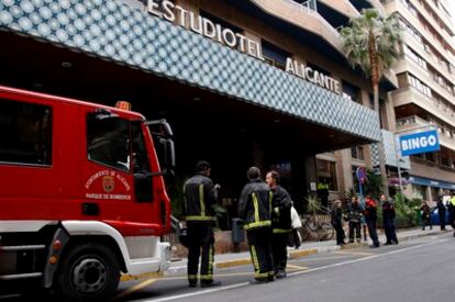 Varios bomberos junto a la entrada del apartotel de Alicante en el que se ha producido un incendio con dos heridos graves y dos leves.