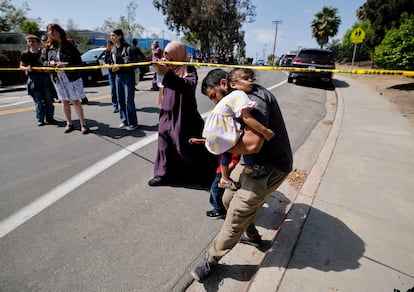 A father walks under yellow tape cordoning off the area while carrying his son in his arms as he leaves the mosque at the site of the shooting at the Islamic Center in San Diego, California.