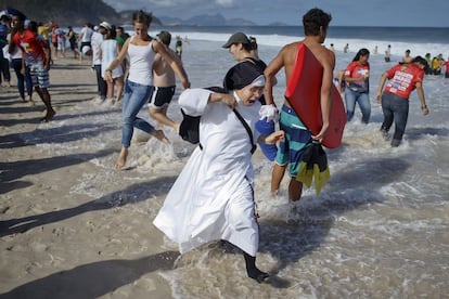 Una monja trata de evitar que el agua la alcance mientras pasea por la playa de Copacabana esta tarde.