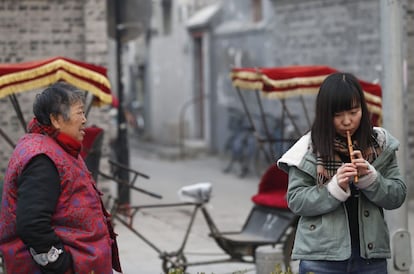 ROL08. Beijing (China), 06/12/2015.- A local resident (L) watches a participant (R) trying to play a flute as part of tasks in a game called 'Hidden City Game' at an open plaza outside the Bell Tower in Beijing, China, 06 December 2015. Game organizers, who aim to provide an alternative experience in learning about Beijing, enjoin local and foreign tourists to participate in games that bring them around various districts while performing fun tasks and answering trivia questions about tourist spots. EFE/EPA/ROLEX DELA PENA