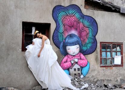 Una novia posa para las fotos de su boda junto a un graffiti pintado en un edificio derribado en Shanghái (China).