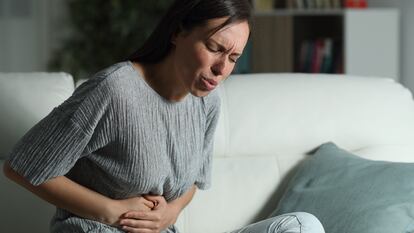 Una mujer está sentada y presenta dolor estomacal.