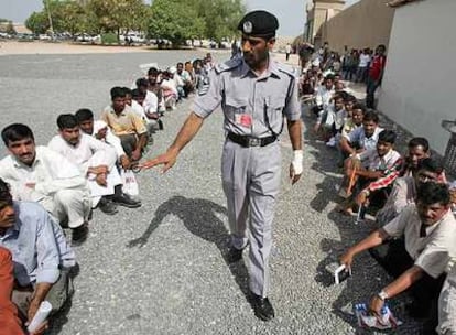 Un policía obliga a colocarse en el suelo a trabajadores, la mayoría asiáticos, que hacen cola frente a la oficina de inmigración de Dubai.