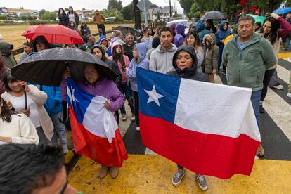 Dos mujeres sostienen banderas de Chile mientras se reúnen personas alrededor de la tenencia policial de lago Ranco, este 6 de febrero.