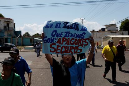 Una mujer sostiene una pancarta que dice "En Zulia lo que tenemos son apagones asegurados" frente a una instalación de la compañía eléctrica nacional Corpoelec durante una protesta contra apagones crónicos y escasez de agua en Maracaibo, 