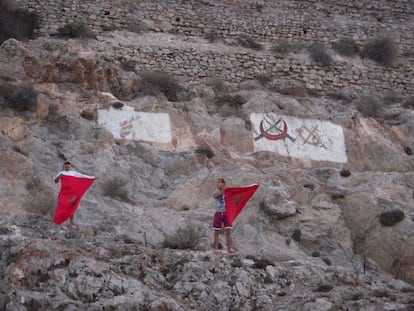 Dos activistas enseñan dos banderas de Marruecos desde el Peñón de Vélez.