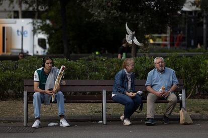 Un joven espera en un banco de plaza Catalunya con una rosa en la mano mientras otras dos personas desayunan un bocadillo.