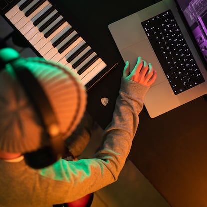 Close-up of an unrecognizable man using a computer and wearing headphones on his head while holding an electric guitar and recording the sound. Musician and technology concept