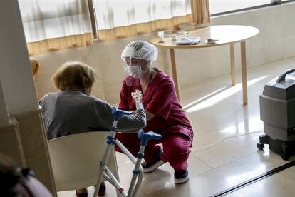 Una trabajadora protegida con un equipo contra los virus atiende a una mujer mayor en la residencia Monte Carmelo, en Madrid.