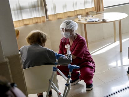 Una trabajadora protegida con un equipo contra los virus atiende a una mujer mayor en la residencia Monte Carmelo, en Madrid.