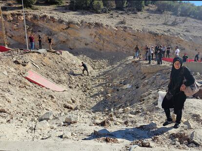 Una mujer lleva sus pertenencias mientras cruza a pie hacia Siria a través de un cráter causado por un ataque aéreo israelí para cortar la carretera entre los puestos de control libaneses y sirios, en el cruce de Masnaa (Líbano).