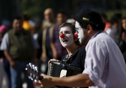 Street musicians with their face painted as clowns, play the accordion and a guitar as pedestrians look on outside the Palacio de Bellas Artes in Mexico City, Mexico August 23, 2015. REUTERS/Henry Romero