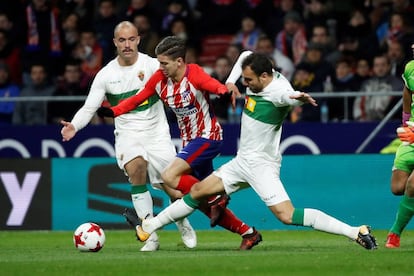 Luciano Vietto (c), intenta llevarse el bal&oacute;n ante los jugadores del Elche, Golobart (i) y Verd&uacute;.