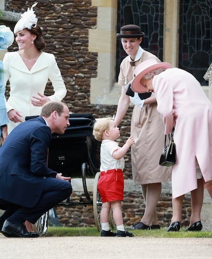 El príncipe Jorge juega con su bisabuela, la reina Isabel II, ante la atenta mirada de su padre, el príncipe Guillermo, y su niñera, María Teresa Turrión Borrallo, después del bautizo de la princesa Carlota (en el carrito), el 5 de julio de 2015. A la izquierda, Kate Middleton.