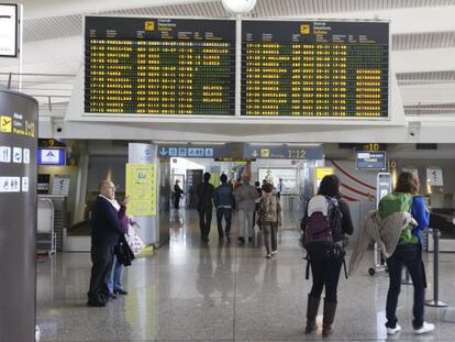 Dos jóvenes con mochilas observan una pantalla informativa en el aeropuerto de Loiu.
