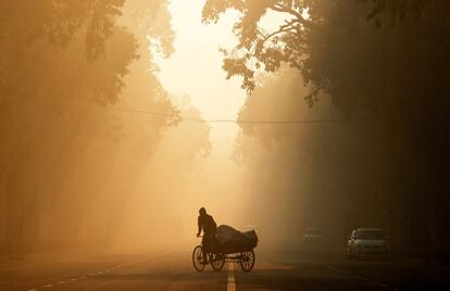 Un hombre montado en un 'rikshaw' recorre una calle envuelta en una neblina debido a la contaminación en Nueva Delhi (India).