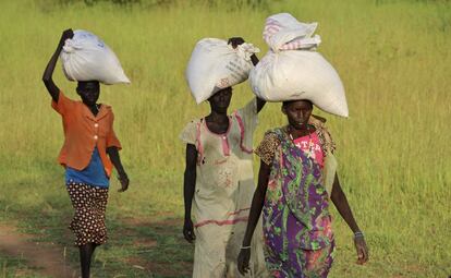 Mujeres sursudanesas regresan a sus casas tras recibir sacos de asistencia alimentaria.