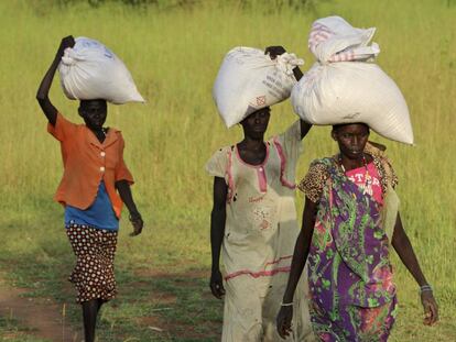 Mujeres sursudanesas regresan a sus casas tras recibir sacos de asistencia alimentaria.